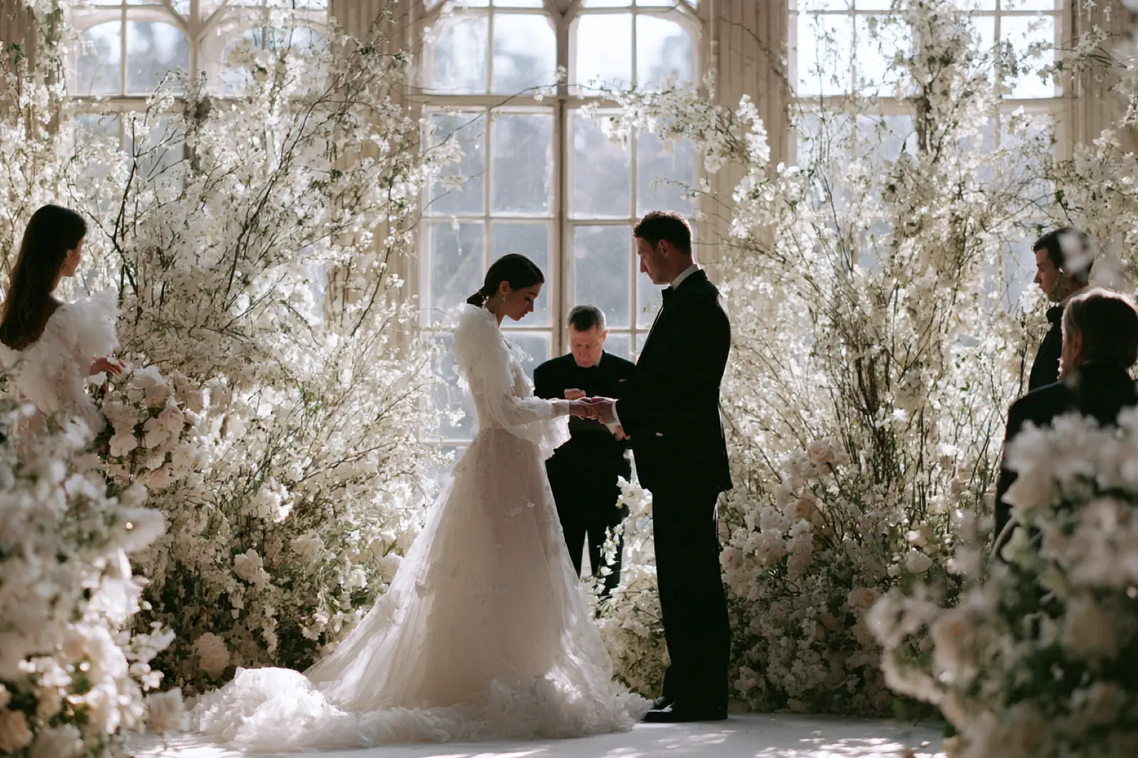 A ceremony among tall white flowers in front of arched windows