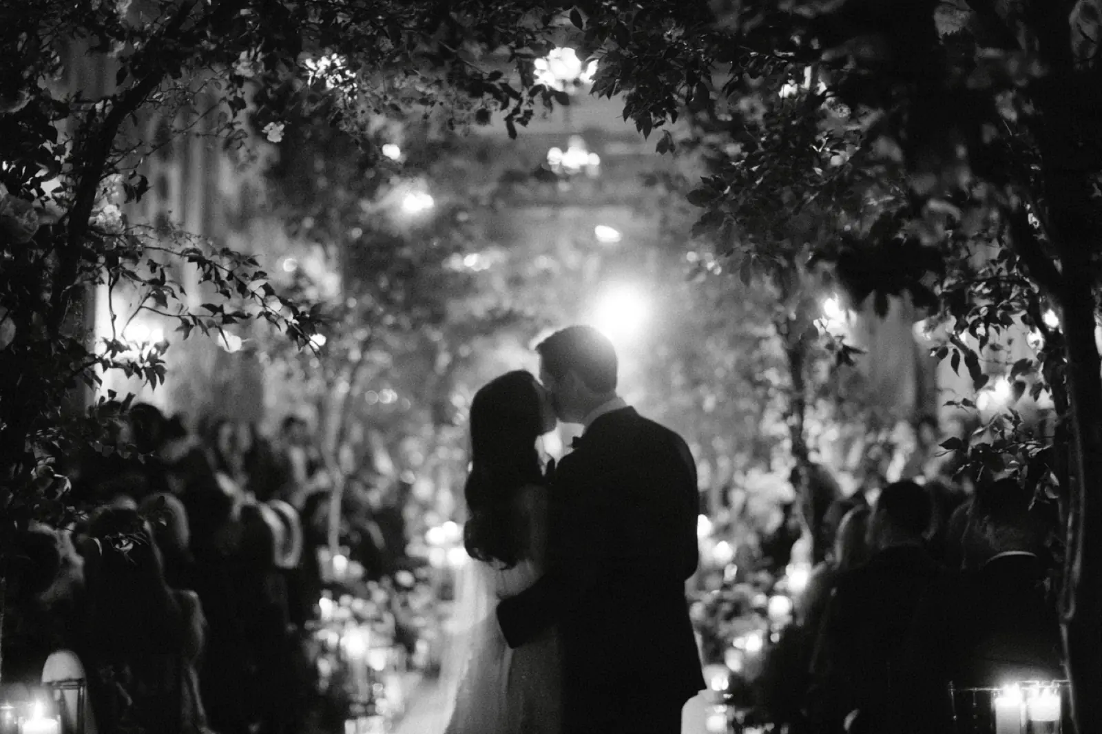 A couple kissing under garden lights, in black and white