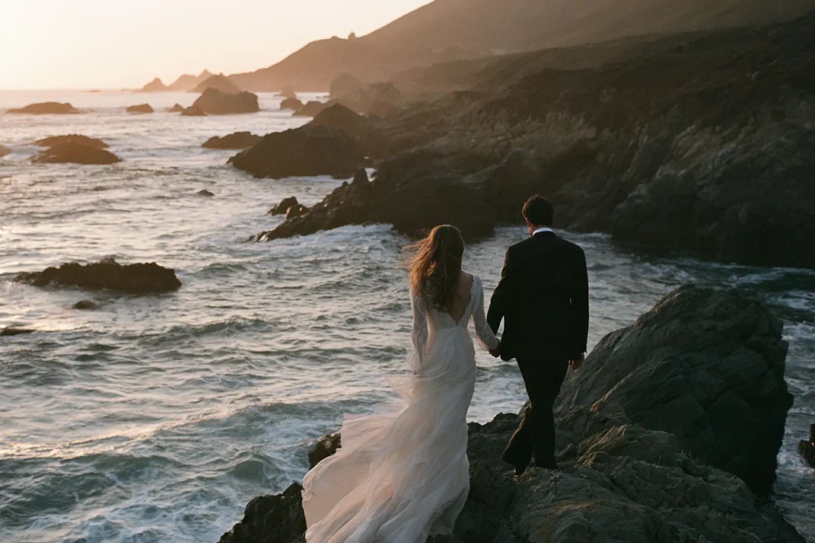 A couple on dark rocks above the surf