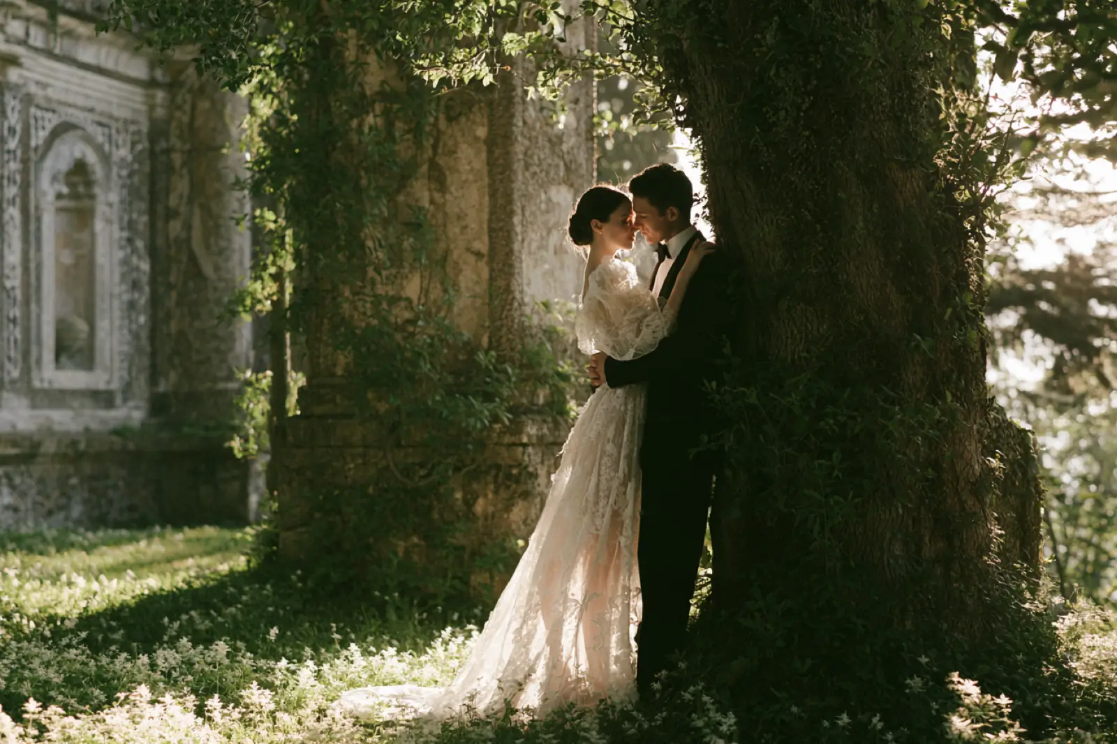 A couple kissing beside an ivy-covered tree and old stone wall