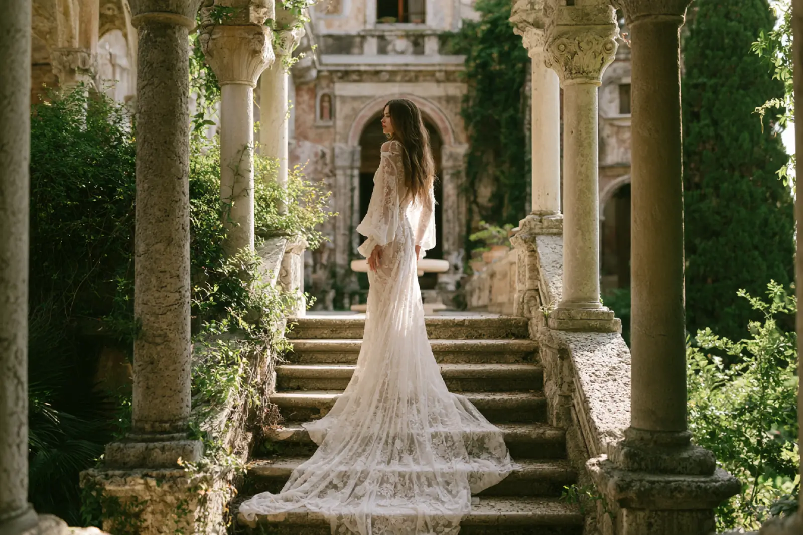 A bride on stone steps between garden pillars