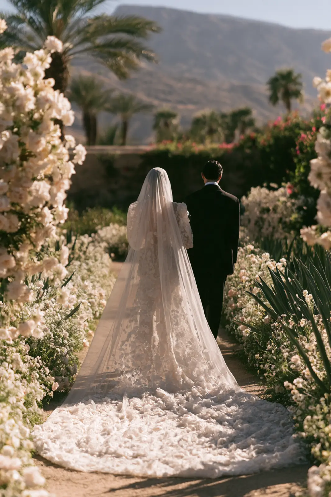 A bride in a long veil walking through a flowering garden