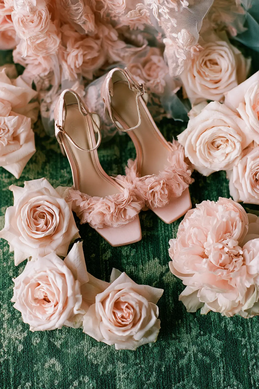 Pink shoes laid among roses on a green cloth