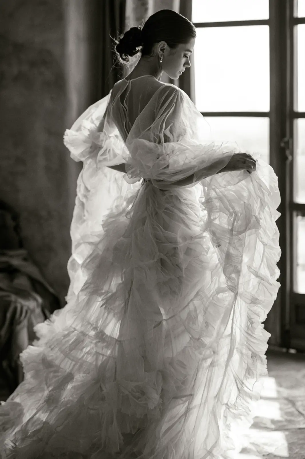 A bride in black and white holding her dress by a tall window