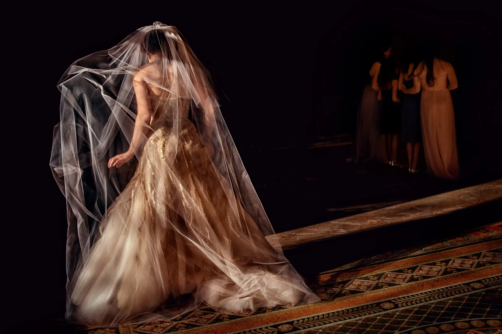 A bride under a long veil in warm light, guests behind her