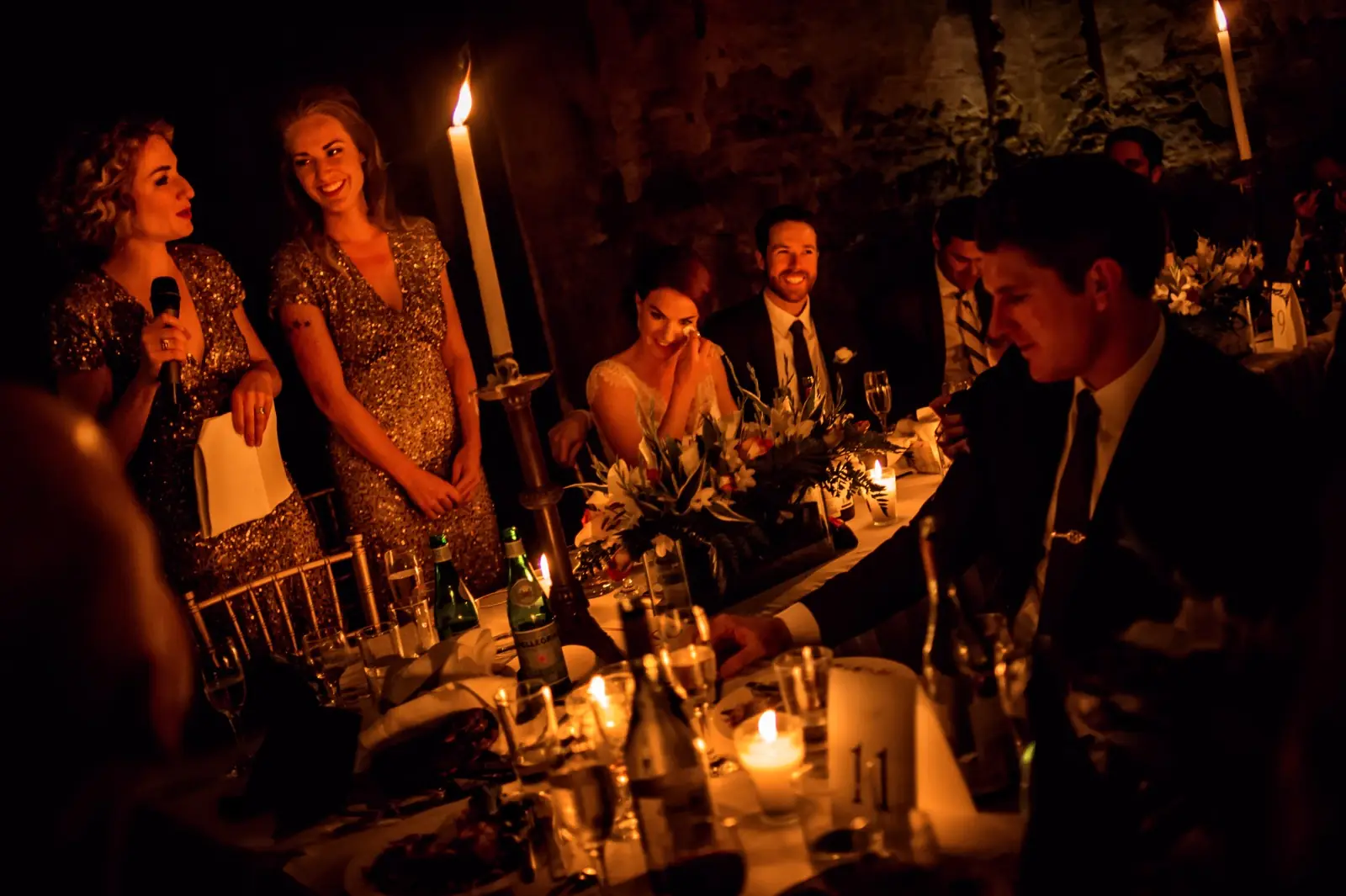 One long candlelit table at night, guests leaning in to talk