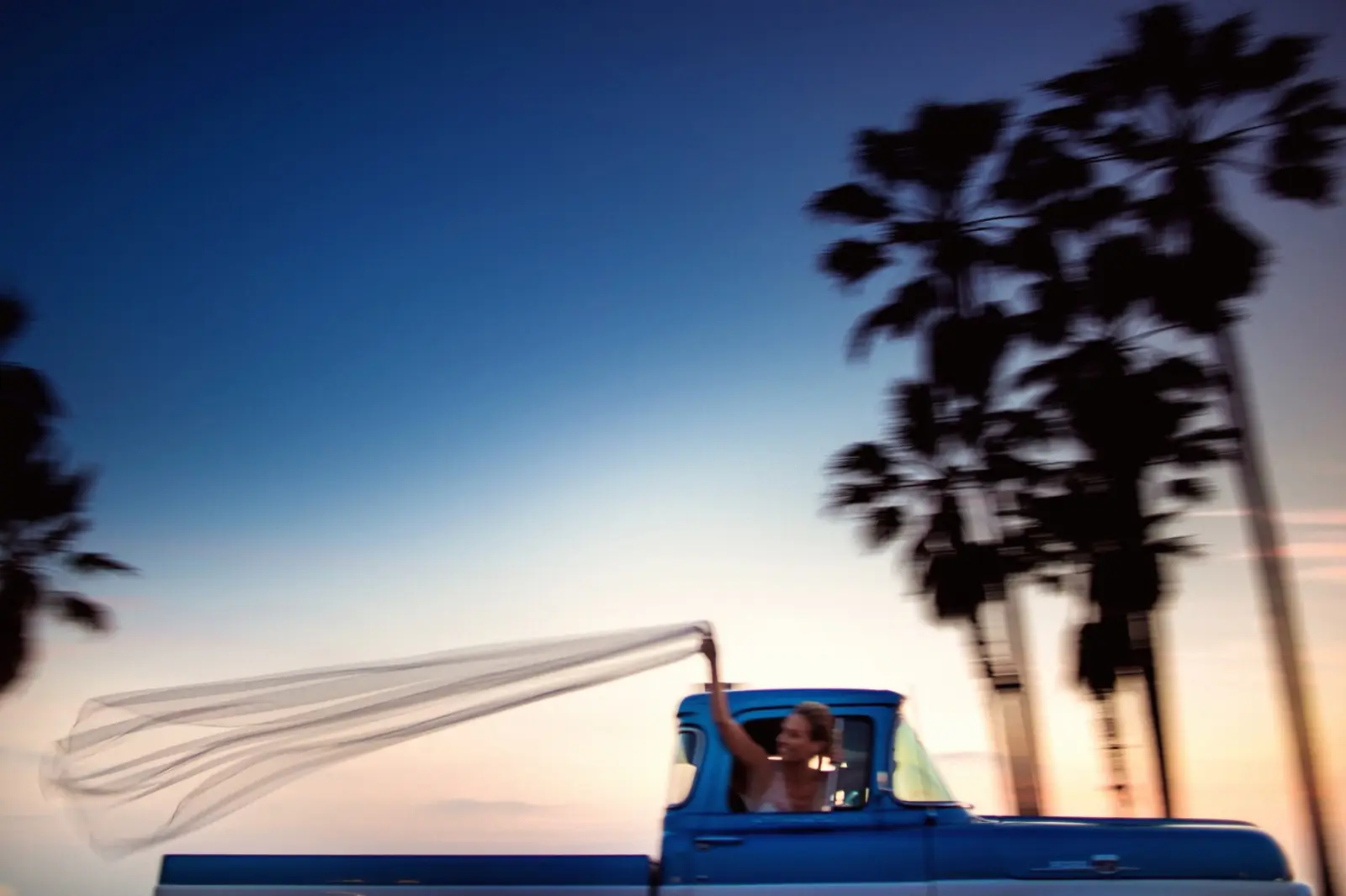 A couple in an open car at sunset, palms against the sky