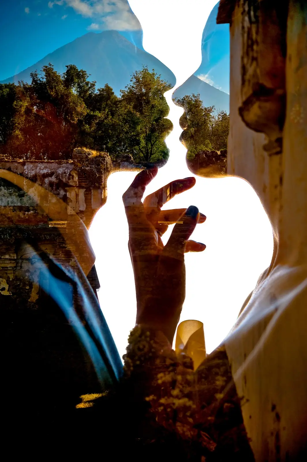 A hand with a ring raised in the bright gap between two silhouetted profiles
